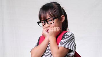 Cute schoolgirl wearing glasses with backpack , she nice-looking, charming and enjoying a good mood on white background in studio. Back to school concept video