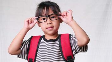 Cute schoolgirl wearing glasses with backpack , she nice-looking, charming and enjoying a good mood on white background in studio. Back to school concept video