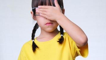 schattig klein meisje dat haar ogen bedekt met handen op een witte achtergrond in de studio. video