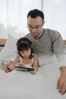 Asian Father Watching Cartoon From Smartphone with Young Daughter in Bedroom photo