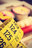 Yellow tailor measuring tape close up with spools of thread in a retro vintage style. Vertical image.