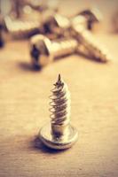 Metal screw close up on a wooden table in a retro vintage style. Vertical image. photo