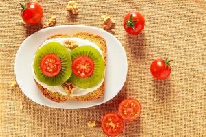 Toast with kiwi, cheese and cherry tomato  on a piece of sackcloth with walnuts and cherry tomatoes around. View from above