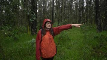 vista frontal de una mujer hispana con una mochila negra y una chaqueta impermeable roja que señala la dirección con el brazo extendido foto