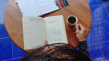 foto de alguien leyendo una novela bebiendo una taza de café solo
