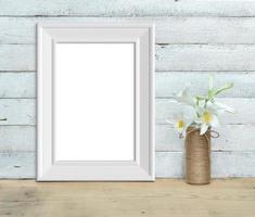 Vertical A4 Vintage White Wooden Frame mockup near a bouquet of lilies stands on a wooden table on a painted white wooden background. Rustic style, simple beauty. 3d render. photo