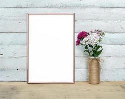 Rose Gold Vertical A4 Frame mocap near a bouquet of sweet-william stands on a wooden table on a painted white wooden background. Rustic style, simple beauty. 3 render photo