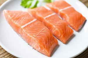 Raw salmon filet with herbs and spices on white plate and wooden background photo