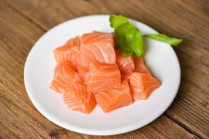 Raw salmon filet cube with herbs and spices on white plate on wooden background photo