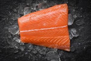 Fresh raw salmon fish steak on ice and dark stone background photo