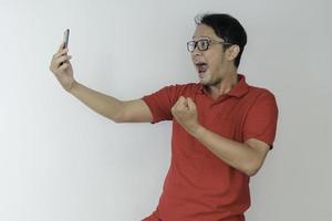 Young Asian man shocked and happy with what he see in the smartphone on isolated grey background. photo