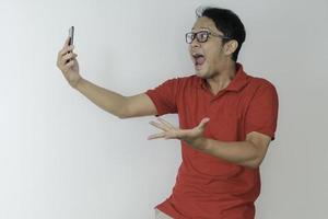 Young Asian man shocked and happy with what he see in the smartphone on isolated grey background. photo