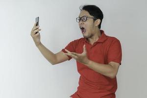 wow, la cara de un joven asiático se sorprendió por lo que vio en el teléfono inteligente con un fondo gris aislado. foto