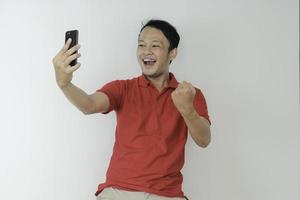 Young Asian man shocked and happy with what he see in the smartphone on isolated grey background. photo