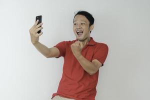 Young Asian man shocked and happy with what he see in the smartphone on isolated grey background. photo