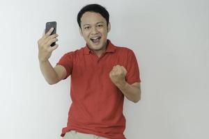 Young Asian man shocked and happy with what he see in the smartphone on isolated grey background. photo