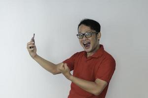 joven asiático conmocionado y feliz con lo que ve en el teléfono inteligente en un fondo gris aislado. foto