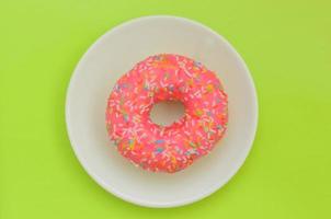One pink glazed donut on white plate on green background, sweet dessert for snack. photo