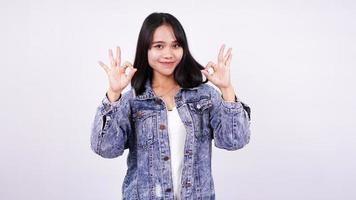 mujer asiática sonriendo con chaqueta de jeans y dedo bien manos arriba con fondo blanco aislado foto