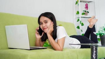 Beautiful  asian women working from home using laptop and calling on phone sleep on chair photo