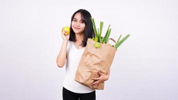 Beautiful Asian woman with paper bag of fresh vegetables and holding fresh lemon photo