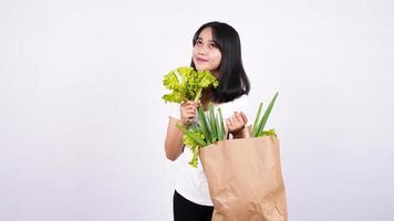 Beautiful Asian woman with paper bag of fresh vegetables and holding fresh lettuce with isolated white background photo