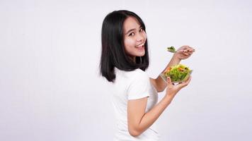 Young asian woman happy eating healthy salad with isolated white background photo