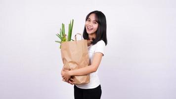 Beautiful asian woman smiling with paper bag of fresh vegetables with isolated white background photo