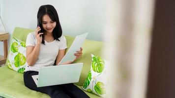 Beautiful  asian women working from home using laptop and calling on phone photo