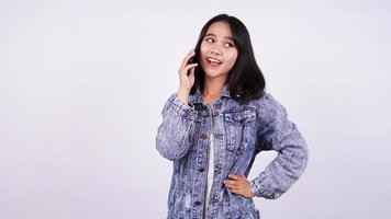 mujer asiática sonriendo con chaqueta de jeans y hablando por teléfono móvil con un fondo blanco aislado foto