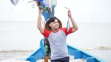 Happy young fisherman on the beach holding his catch fish and shows in front of his boat photo