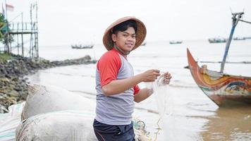 Portrait of a young male fisherman preparing a fishing net in beach photo