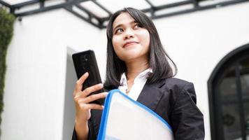 Beautiful young asian business woman in suit standing at cafe with phone and Brown envelope photo