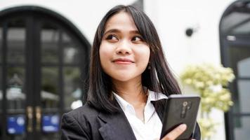 hermosa joven mujer de negocios asiática en traje de pie en el café con teléfono y sobre marrón foto