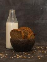 Bottle with milk and sliced rye bread on a dark background.