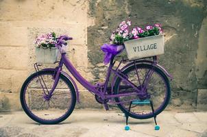 Watercolor drawing of Vintage violet bike bicycle with box of flowers in front of stone wall on narrow stone street photo
