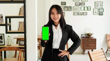 Beautiful young asian business woman in suit standing at cafe with green screen phone photo