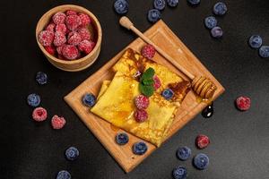 Top view, thin pancakes with berries, mint leaves and honey, dark background photo