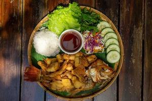 Top View Food Photo of Fried Tilapia Fish on a Bamboo Plate with Sliced Cucumber, Mixed Salad, Rice and Tamarind Sauce at a Vietnamese Restaurant