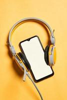 auriculares y smartphone con pantalla en blanco sobre fondo amarillo foto
