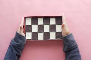 holding a dark and white chocolate in a box on pink background photo