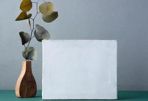 blank canvas frame with eucalyptus in wood vase on green table photo