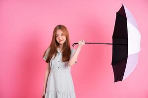 Young Asian woman holding umbrella on pink background photo