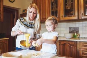 Happy smiling mom in the kitchen bakes cookies with her daughter. photo