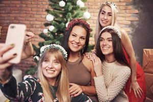 Portrait of four smiling girl with corolla on the head make selfie photo. New year's feeling. Merry christmas photo
