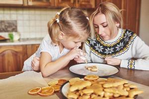 Confectionery workplace with women's hands decorating Christmas cookies. Home bakery, sunny sweet, winter holidays. photo