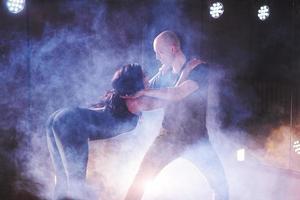 hábiles bailarines actuando en la habitación oscura bajo la luz y el humo del concierto. pareja sensual realizando una danza contemporánea artística y emocional foto