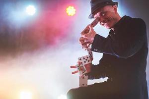 Magician showing trick with playing cards. Magic or dexterity, circus, gambling. Prestidigitator in dark room with fog photo