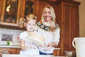 Happy smiling mom in the kitchen bakes cookies with her daughter. photo