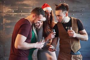 alegres viejos amigos se comunican entre sí y miran el teléfono, con copas de champán en la fiesta de año nuevo. concepto de entretenimiento y estilo de vida. personas conectadas wifi